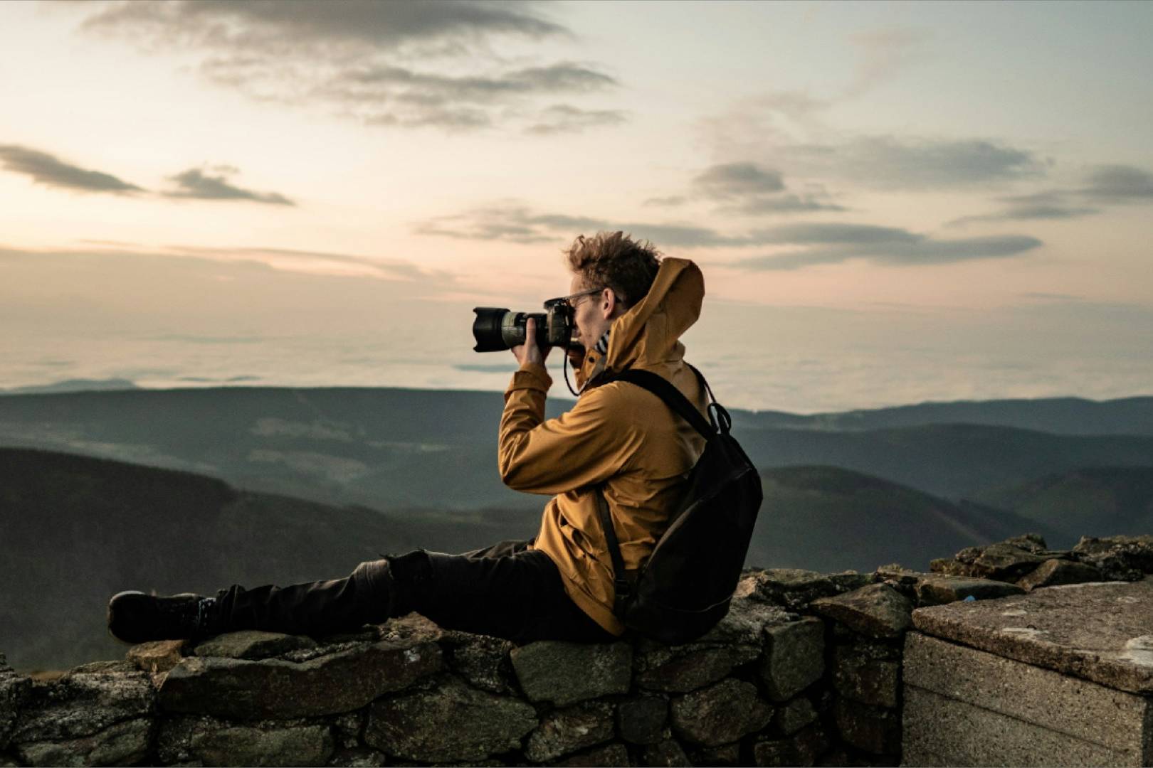 man in brown jacket taking photo of mountain during daytime